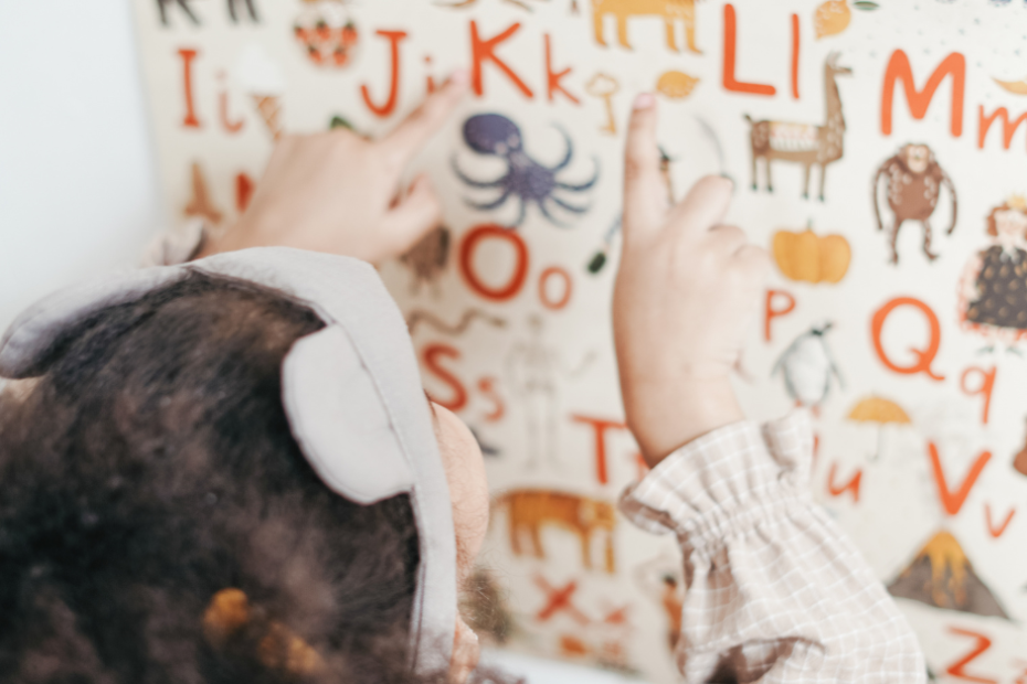 Dziecko zwrócone twarzą do tablicy, na literki na której znajdują duże i małe literki oraz zwierzęta.