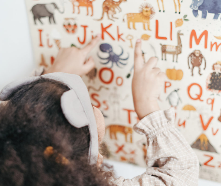 Dziecko zwrócone twarzą do tablicy, na literki na której znajdują duże i małe literki oraz zwierzęta.