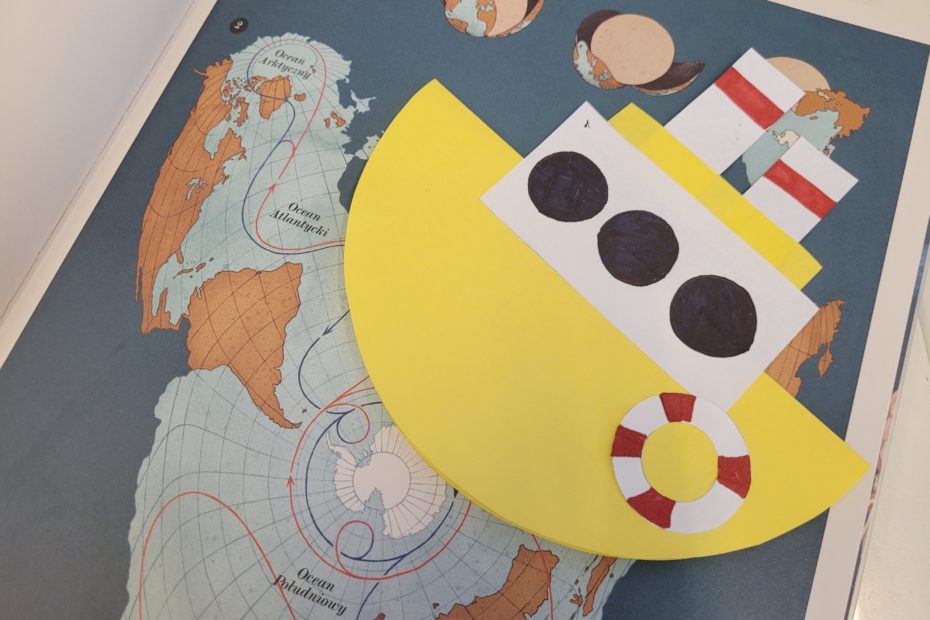 Na książce z mapą ułożony żółty statek z papieru.