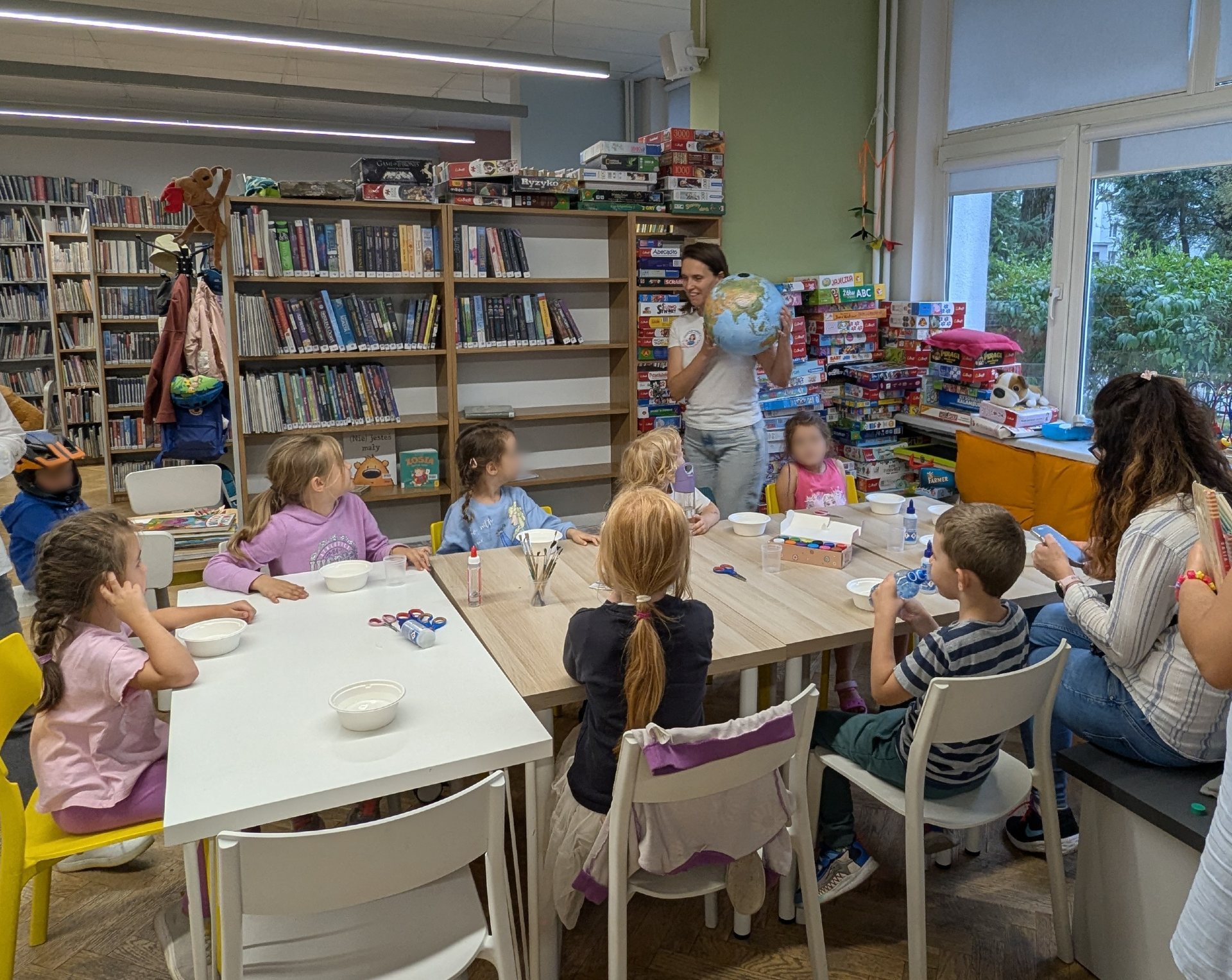 zdjecie z warsztatów "to nie magia, to nauka - na tropie przygody" we wnętrzu wypożyczalni nr 138 i biblioteki dla dzieci nr XV przy ul. Broniewskiego 9a. dzieci i dorośli przy stole wykonujący prace plastyczne