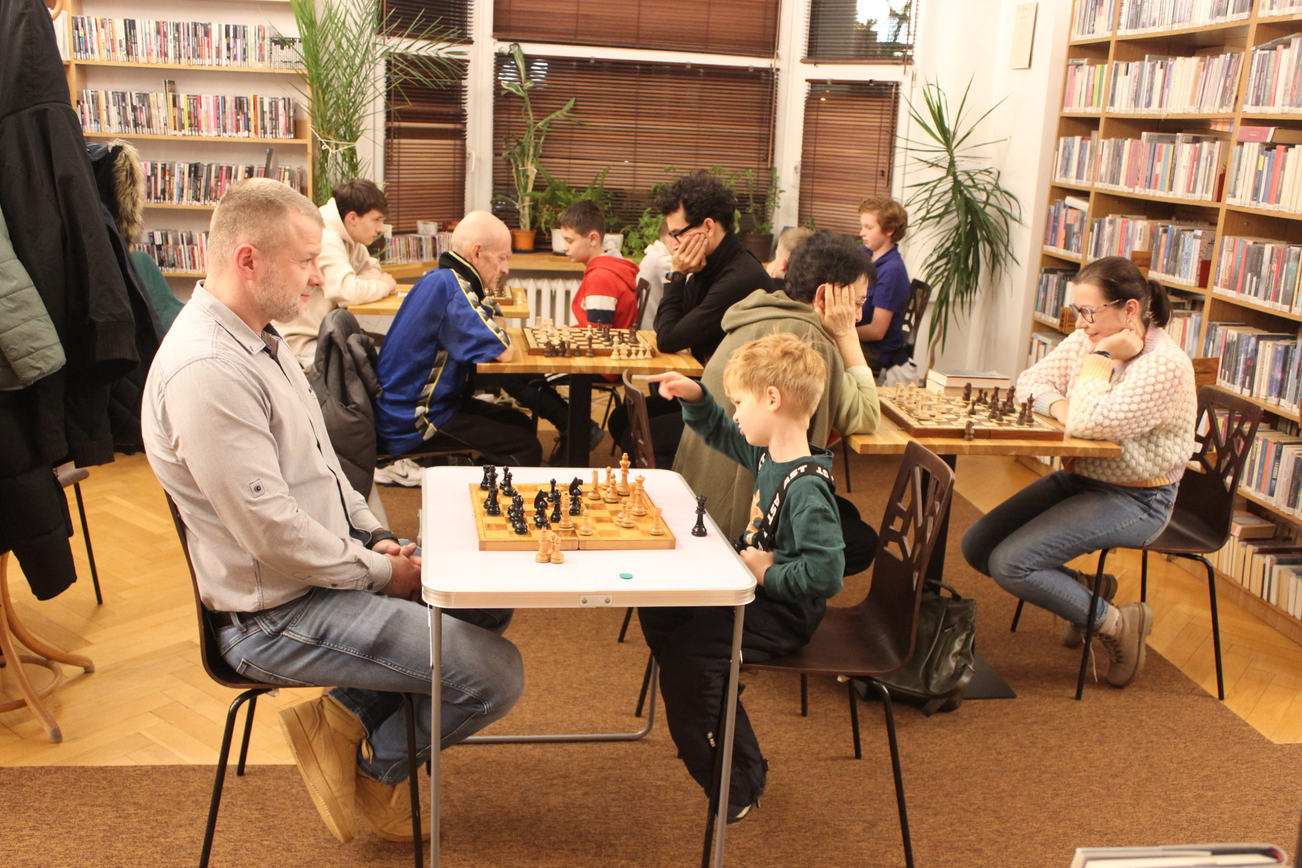 grafika wyróżniająca przedstawiająca uczestników kółka szachowego. uczestnicy siedzą przy stołach i grają w szachy