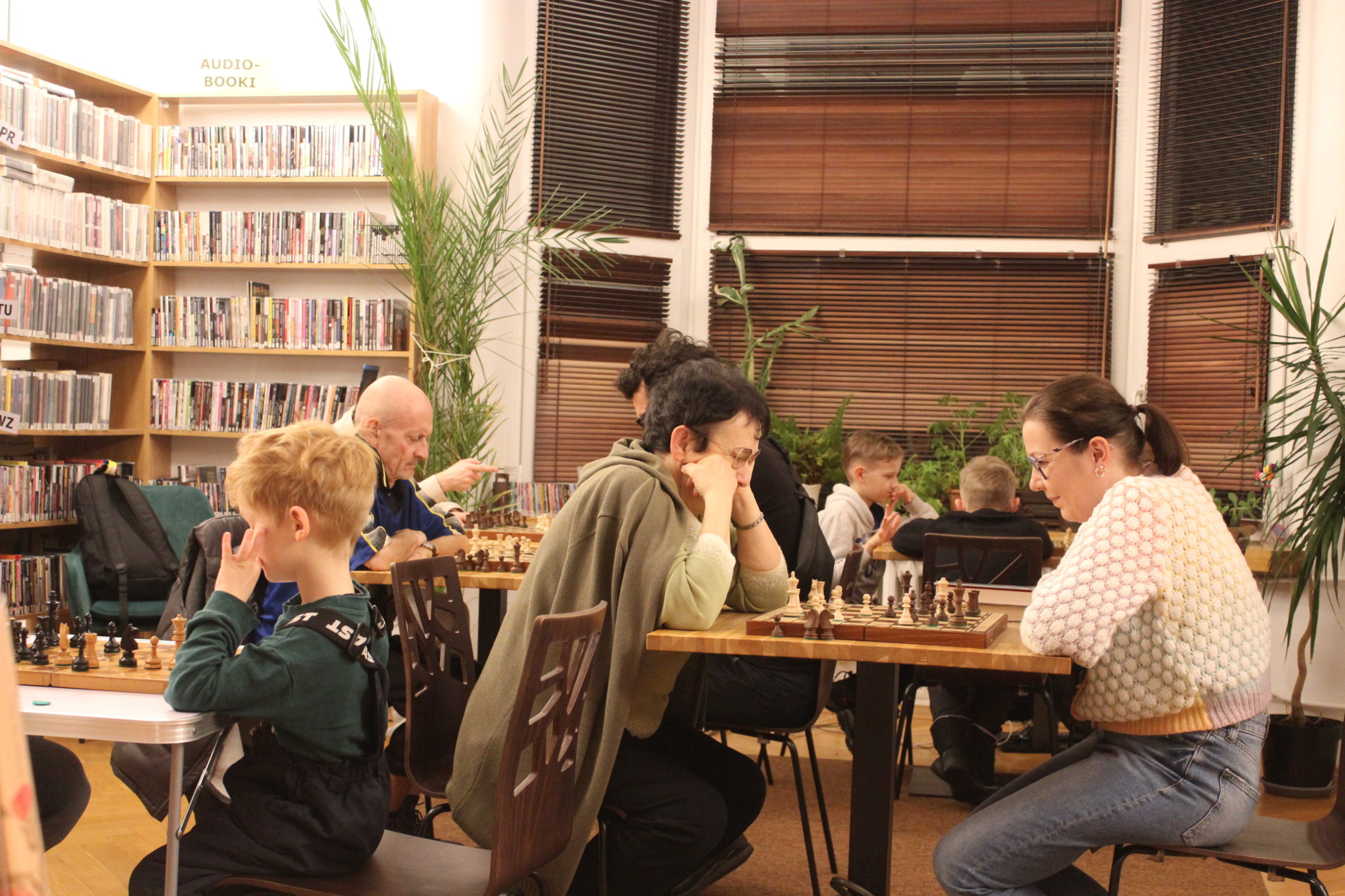 grafika wyróżniająca przedstawiająca uczestników kółka szachowego. uczestnicy siedzą przy stołach i grają w szachy