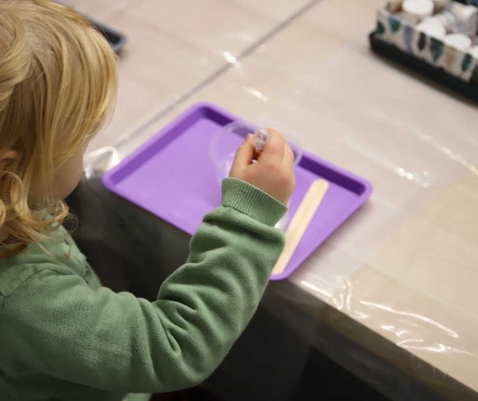 Dziecko z jasnymi włosami robi eksperyment nad fioletową tacką.