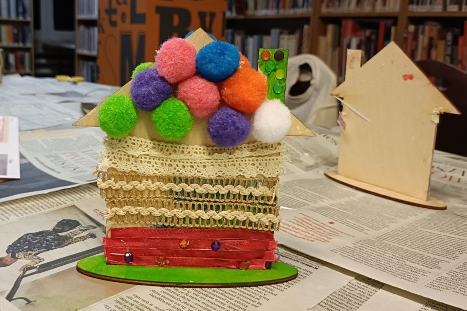 zdjęcie przedstawiający płaski drewniany domek z kolorowymi pomponami-końcowy efekt warsztatów