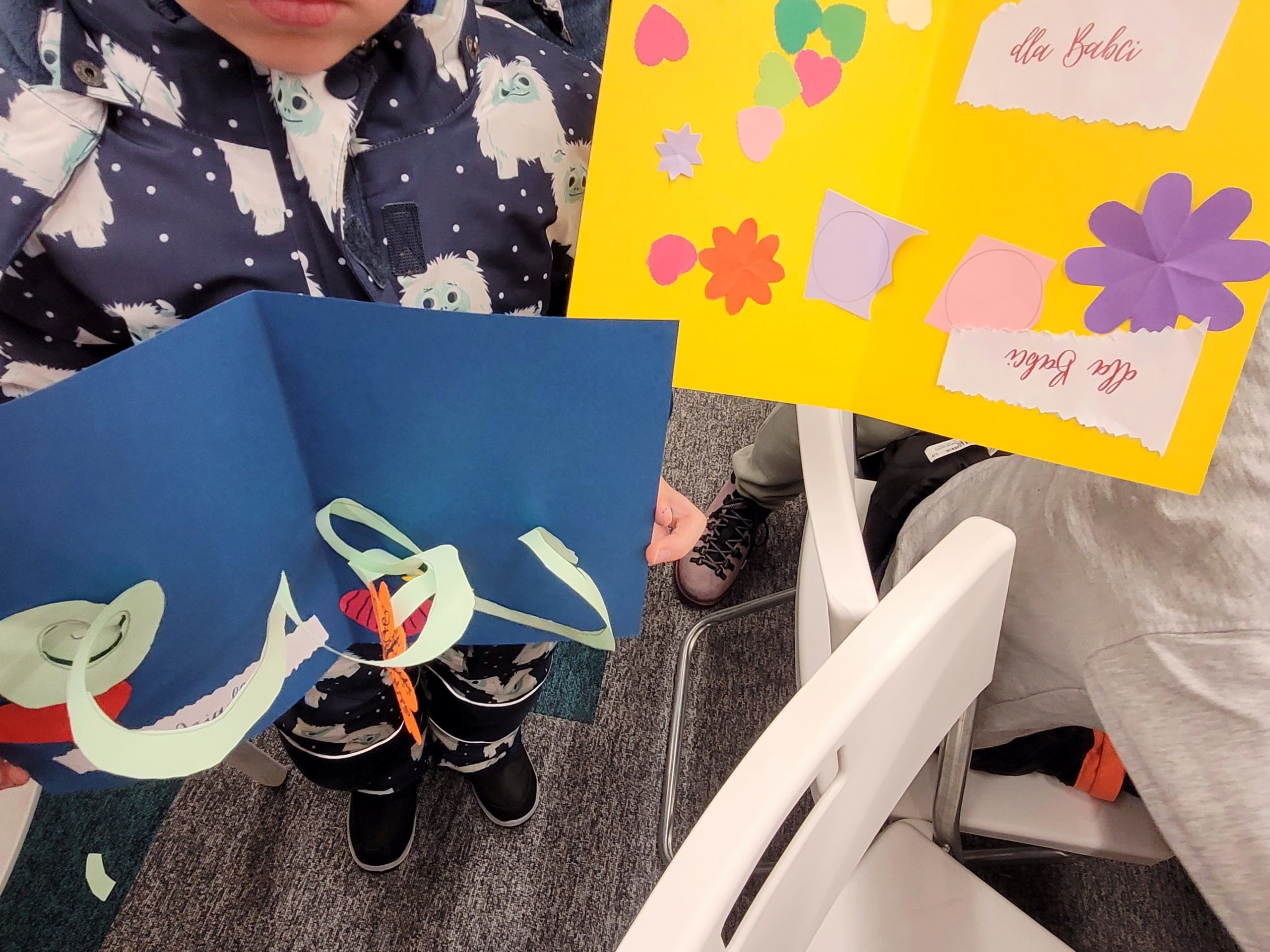 Dzieci trzymają kolorowe kartki (niebieska i żółta). Na jednej naklejki z napisem "dla Babci"