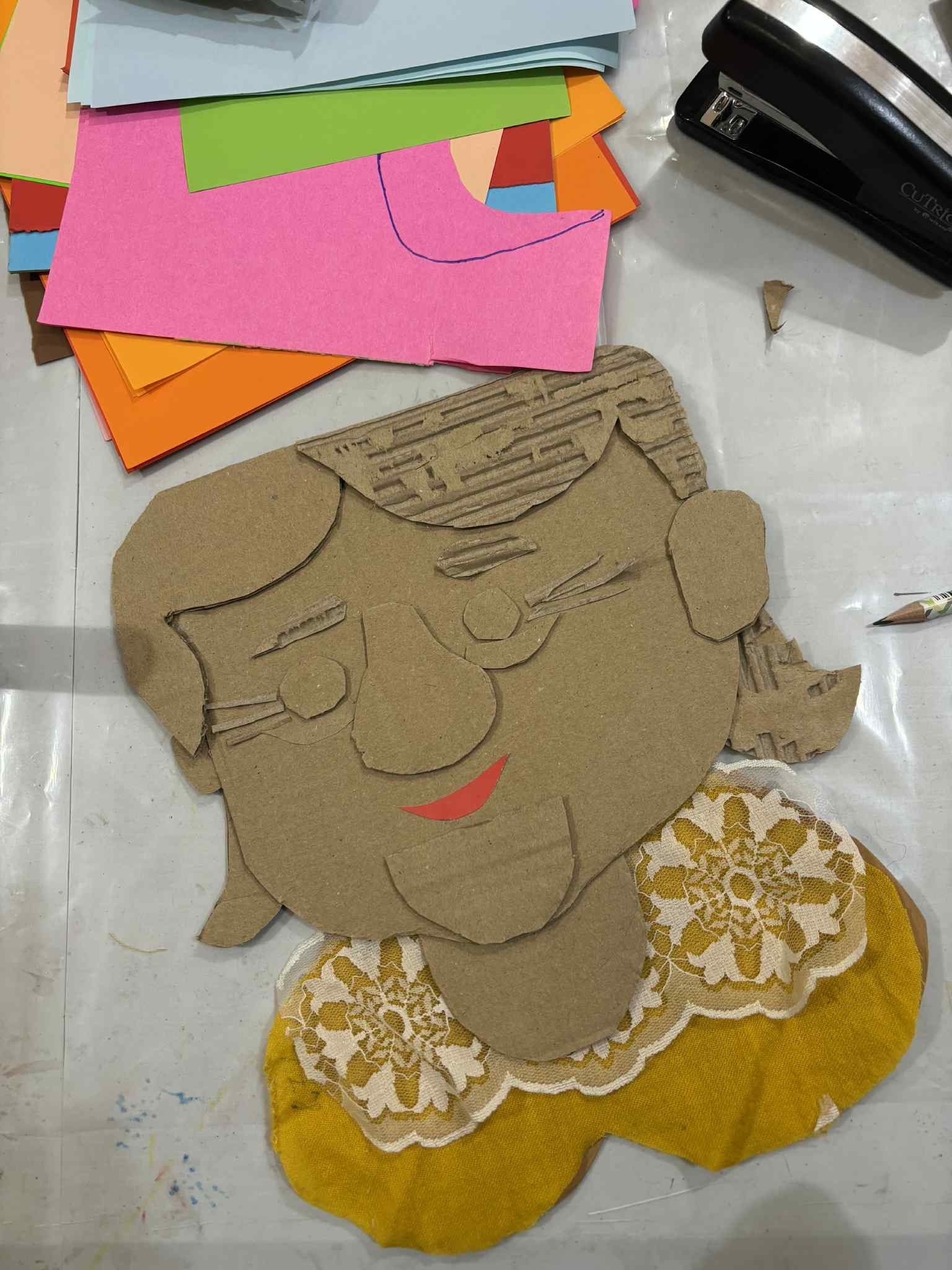 grafika przedstawiająca skończoną prace z zajęć artystycznych, która przedstawia portret babci wykonany z kartonu, materiału i koronki