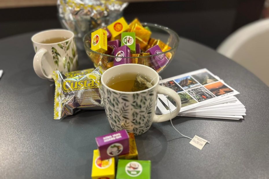 grafika przedstawiająca zdjęcie ze spotkania podróżniczego. Przedstawia słodycze przywiezione z Azji i dwa kubki zielonej herbaty. Prowadzący częstowali czytelników tymi słodyczami.