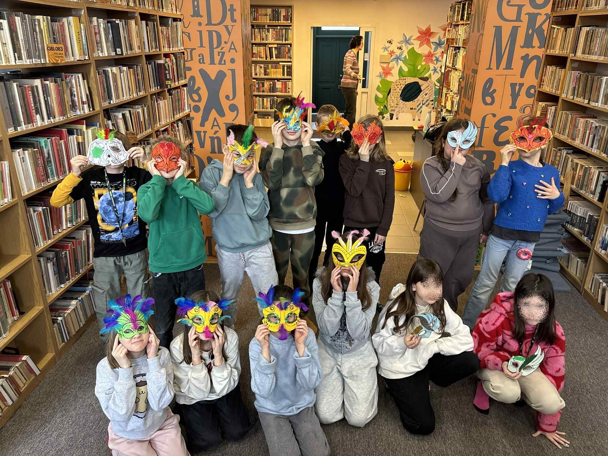 zdjęcie przedstawia grupę dzieci, które prezentują zrobione przez siebie brazylijskie maski karnawałowe z piórami. Zasłaniają nimi swoje twarze.