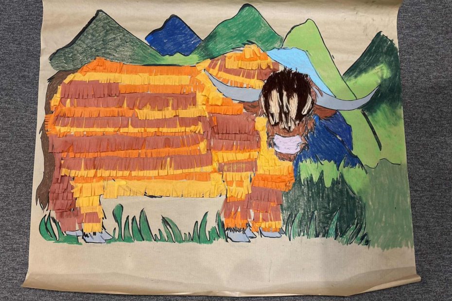 zdjęcie przedstawia ukończoną pracę plastyczną, która została wykonana podczas warsztatów podróżniczych. Tematem była szkocka krowa, która dzici wykonały z pomarańczowej i brążowej krepiny, pokolorowały kredkami. Całość została zrobiona na szarym papierze.