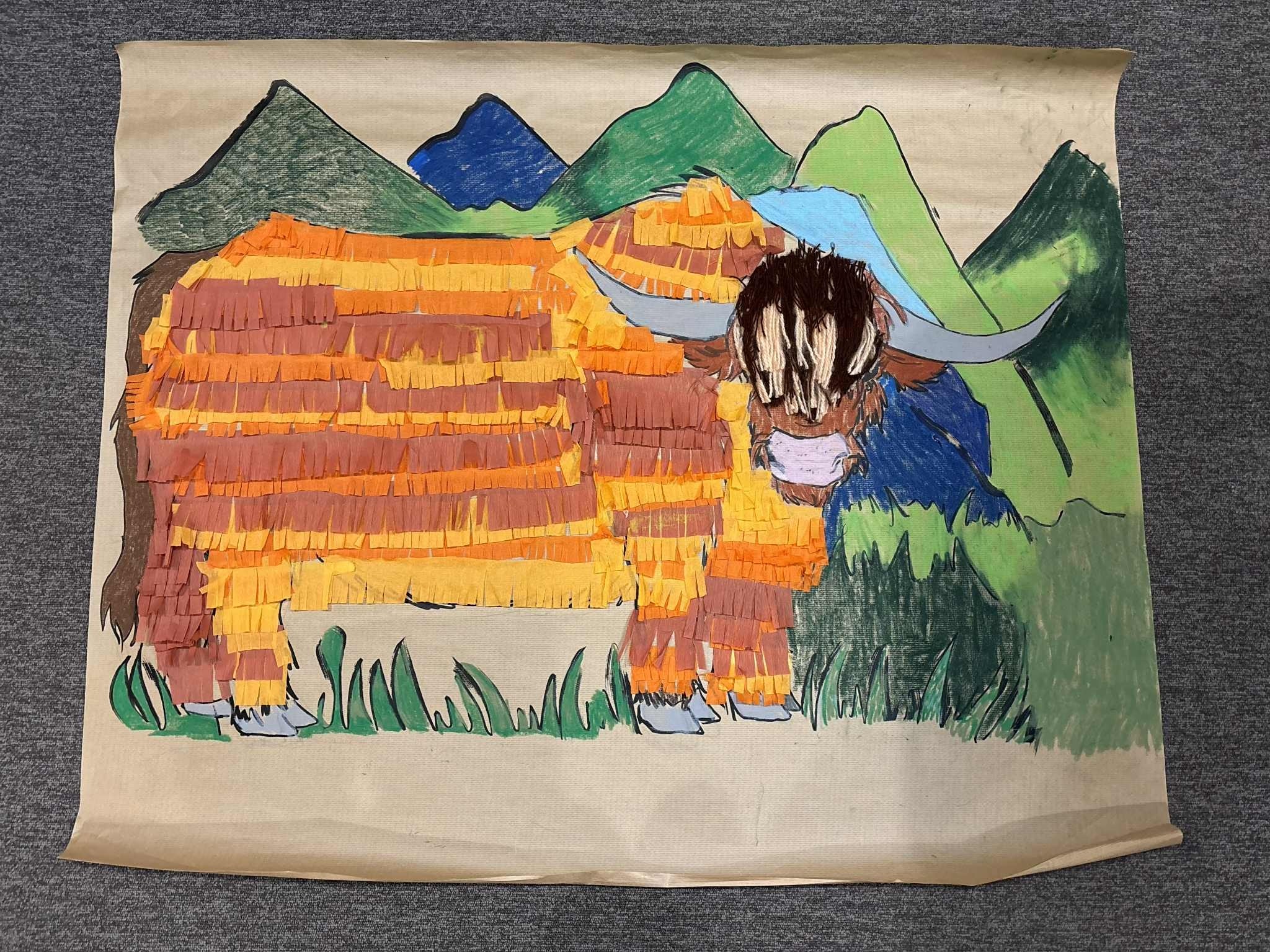 zdjęcie przedstawia ukończoną pracę plastyczną, która została wykonana podczas warsztatów podróżniczych. Tematem była szkocka krowa, która dzici wykonały z pomarańczowej i brążowej krepiny, pokolorowały kredkami. Całość została zrobiona na szarym papierze.