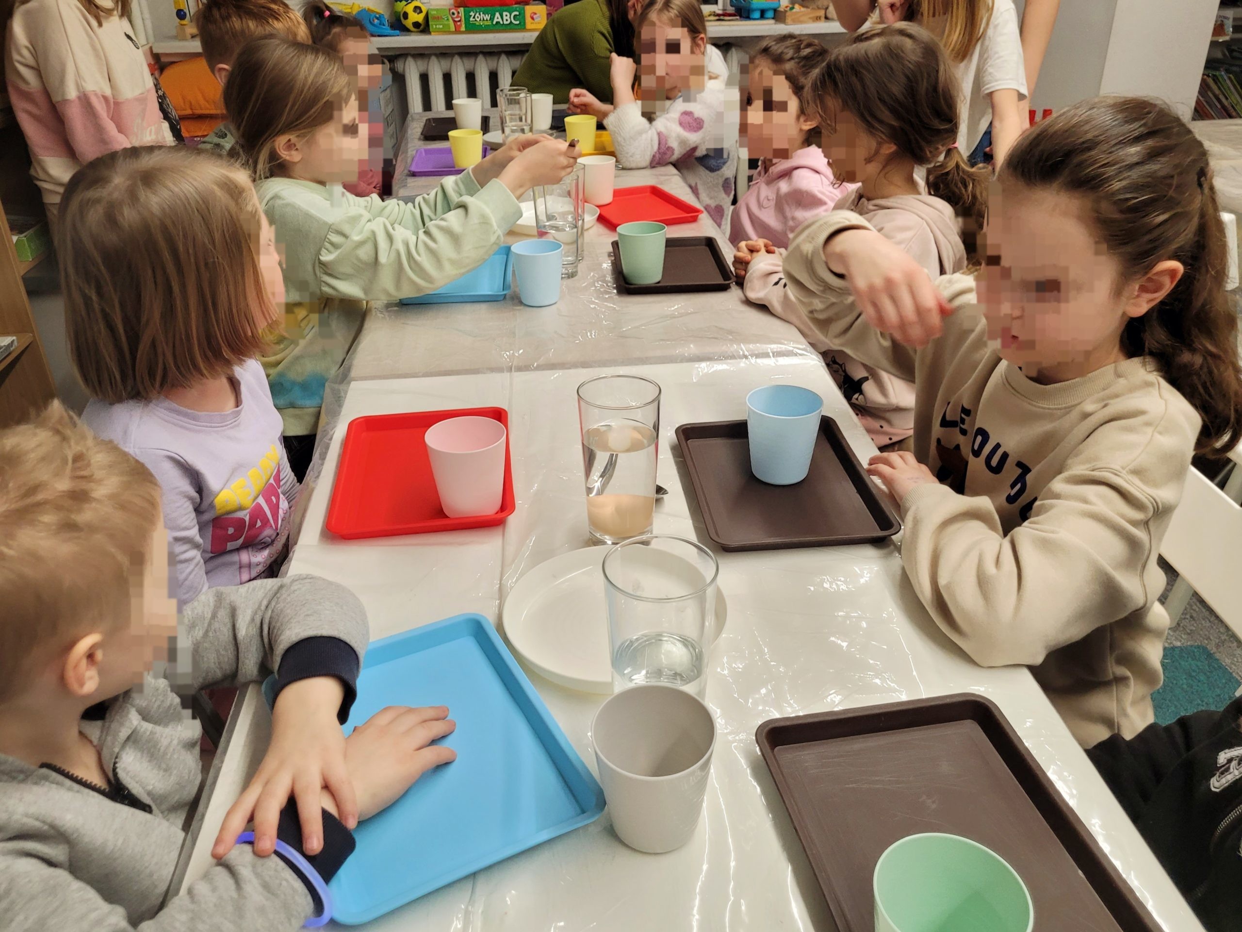 Dzieci skupione wokół stołu wykonują proste doświadczenia z jajkami i wodą podczas zajęć edukacyjnych w bibliotece.