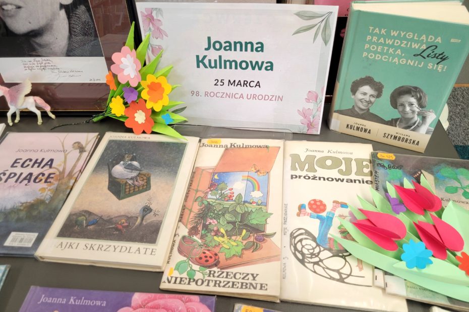 Fragment wystawy: książki Joanny Kulmowej dla dzieci, portret autorki oraz dekoracje z kolorowego papieru.