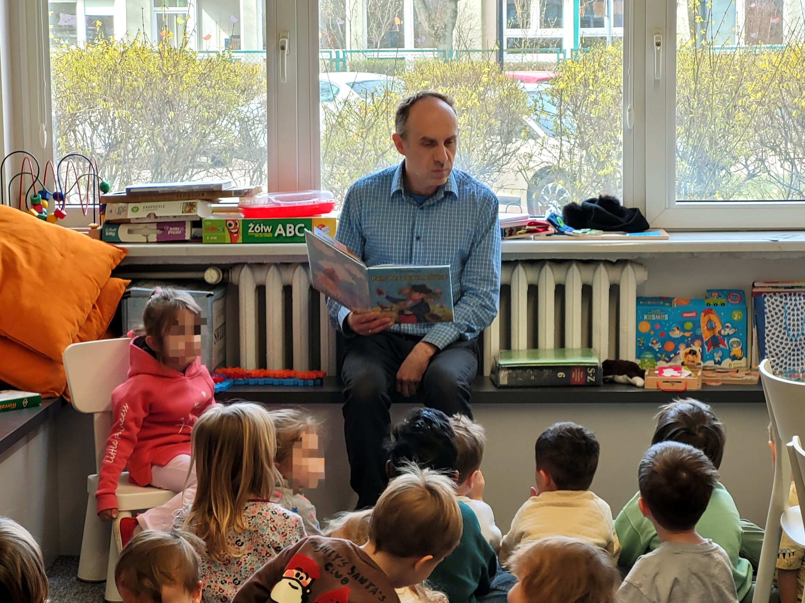 Zbliżenie na bibliotekarza czytającego książkę dzieciom podczas spotkania czytelniczego w bibliotece.