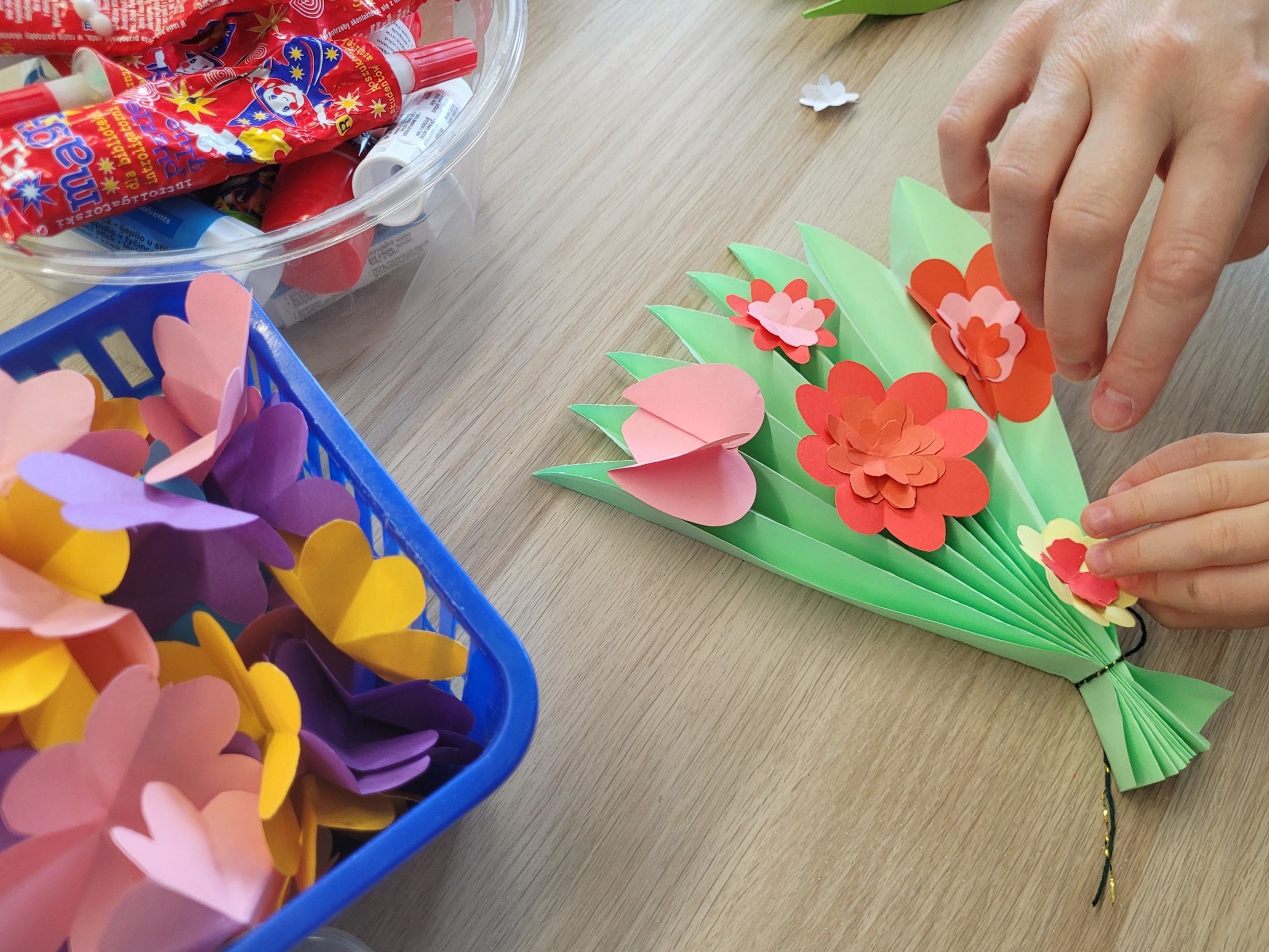 Gotowe prace plastyczne dzieci: papierowe bukiety z kolorowymi kwiatami ułożone na stole.