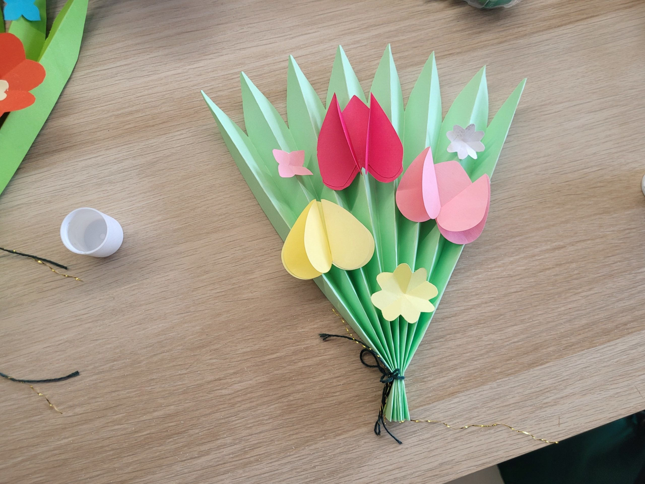 Pojedyncza praca plastyczna dziecka – zielony papierowy bukiet ozdobiony kolorowymi kwiatami.